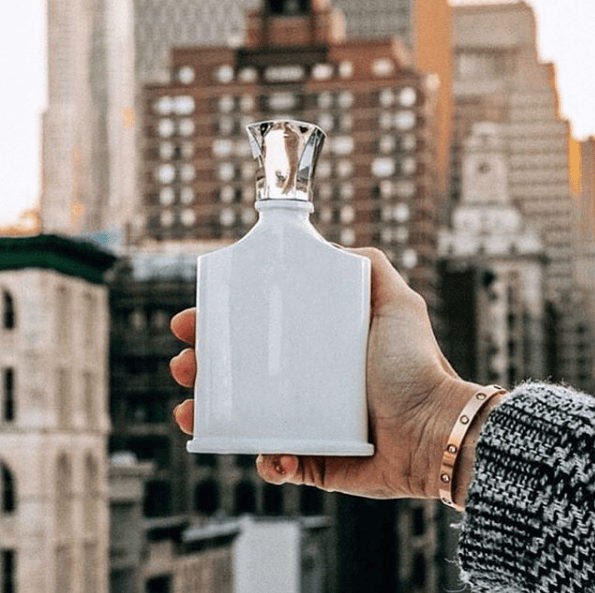 Hand holding a perfume bottle in front of an urban landscape
