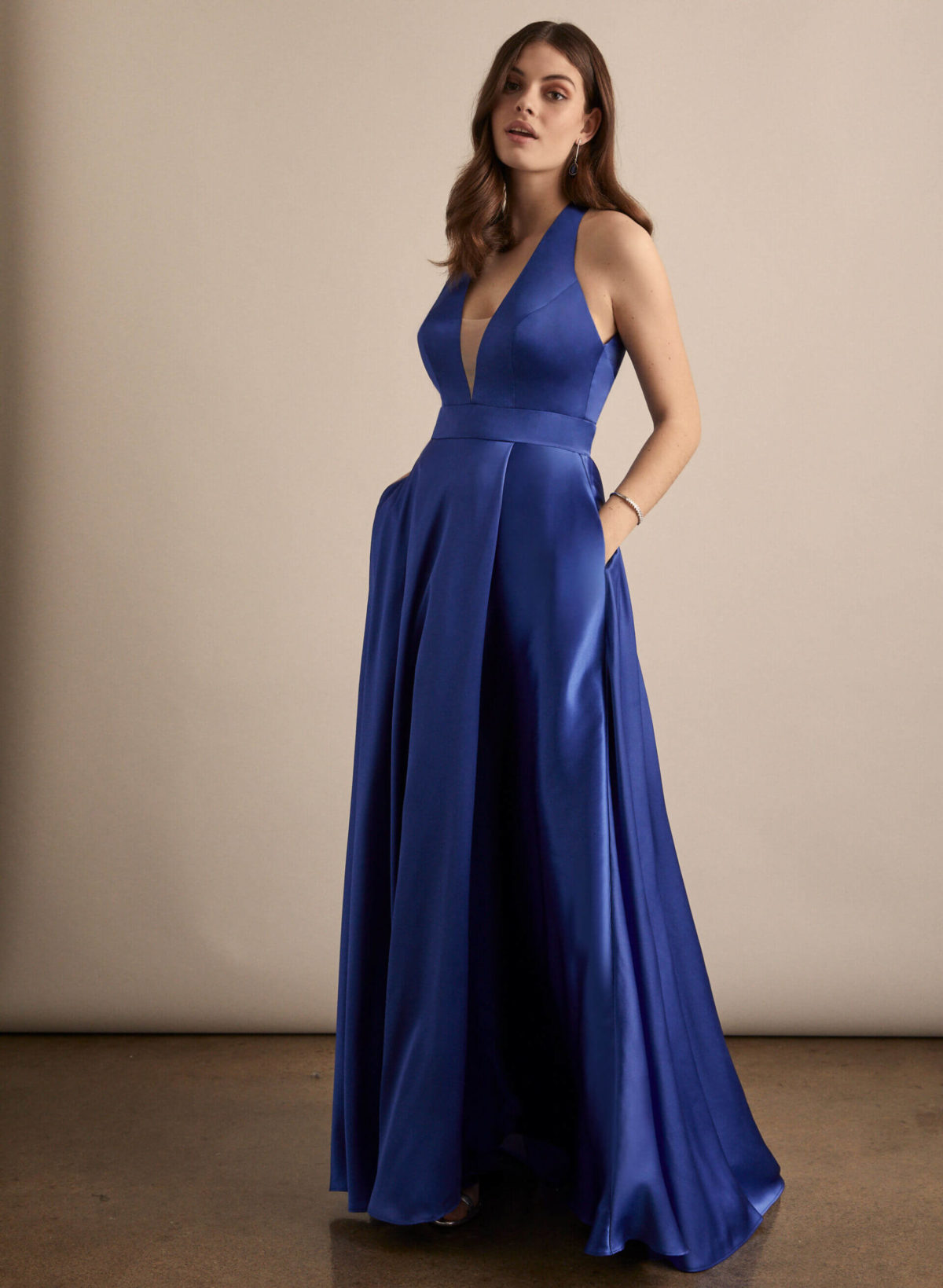 A young woman wearing a V-neck satin prom dress with pockets.