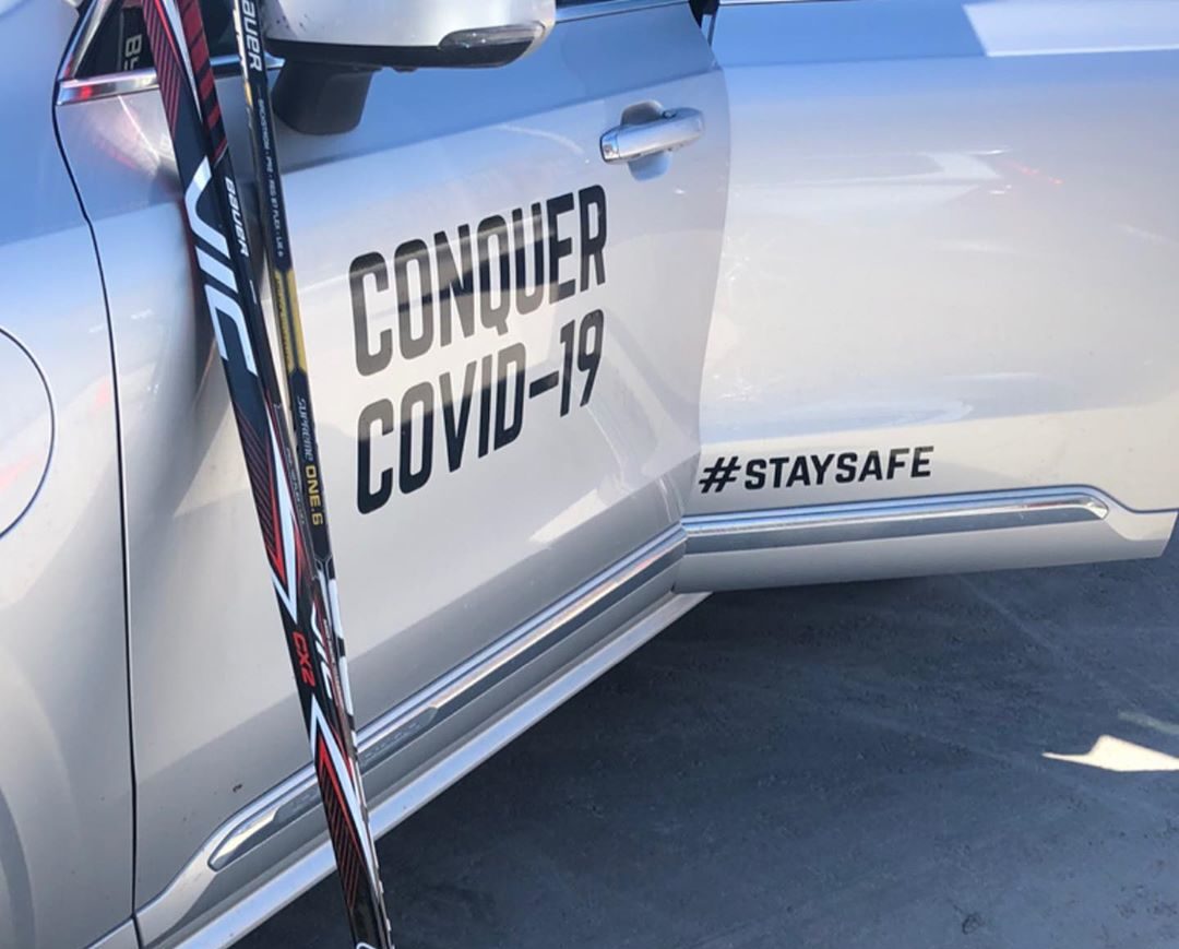 A car with Conquer COVID-19 and stay safe printed on the side.