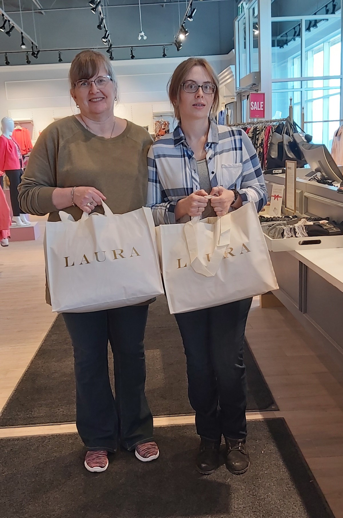 A mother and daughter holding donated clothing items at a Laura store.