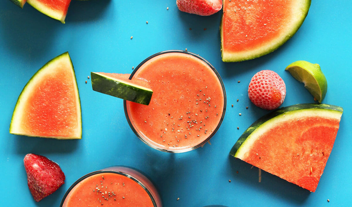 A strawberry watermelon chia seed smoothie surrounded by fruit ingredients.
