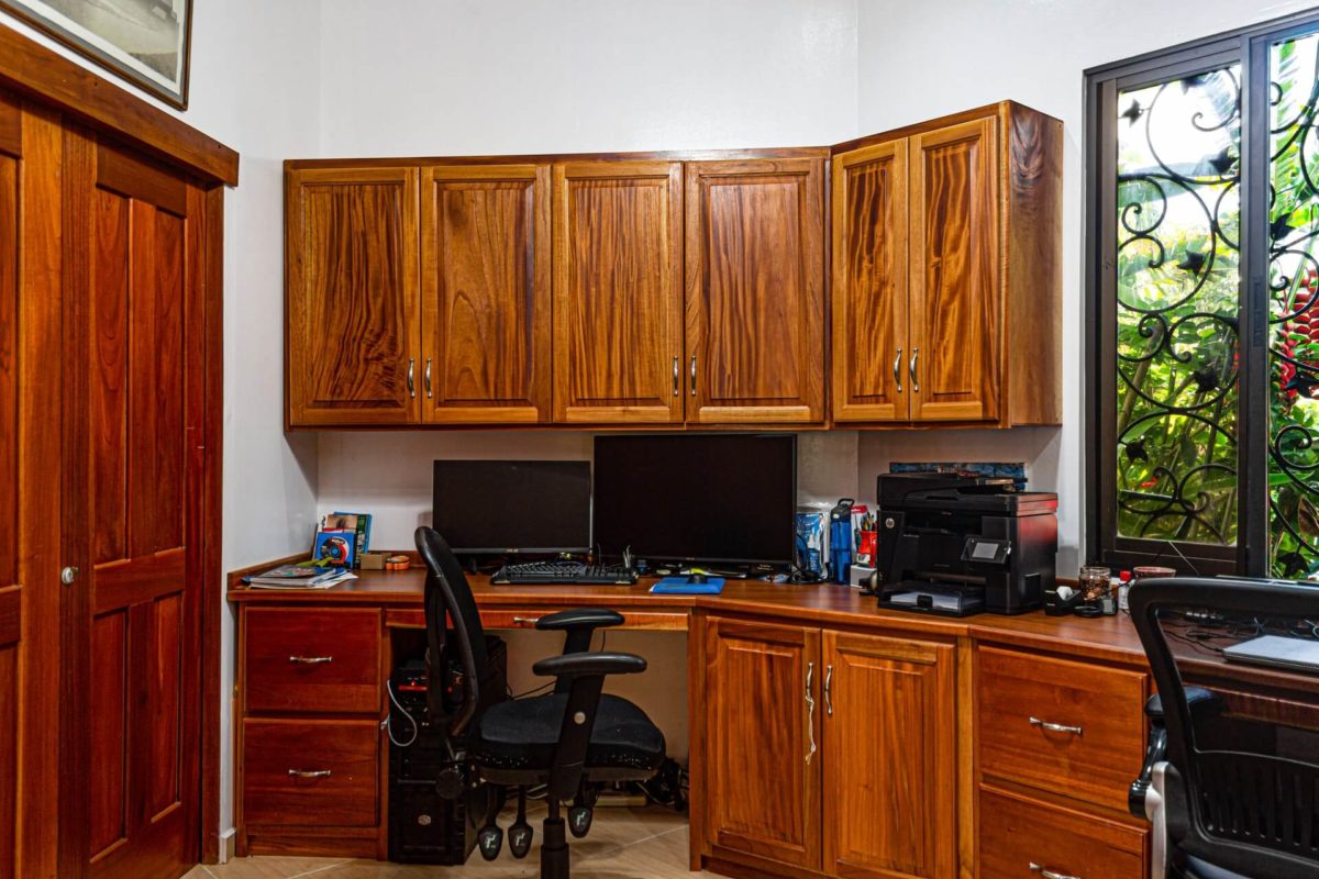 A home office with a computer, printer, desk chair, and cabinetry.