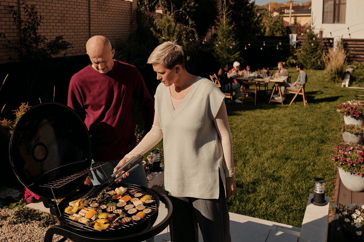 A backyard barbecue party with 2 hosts at the barbecue and guests in the background