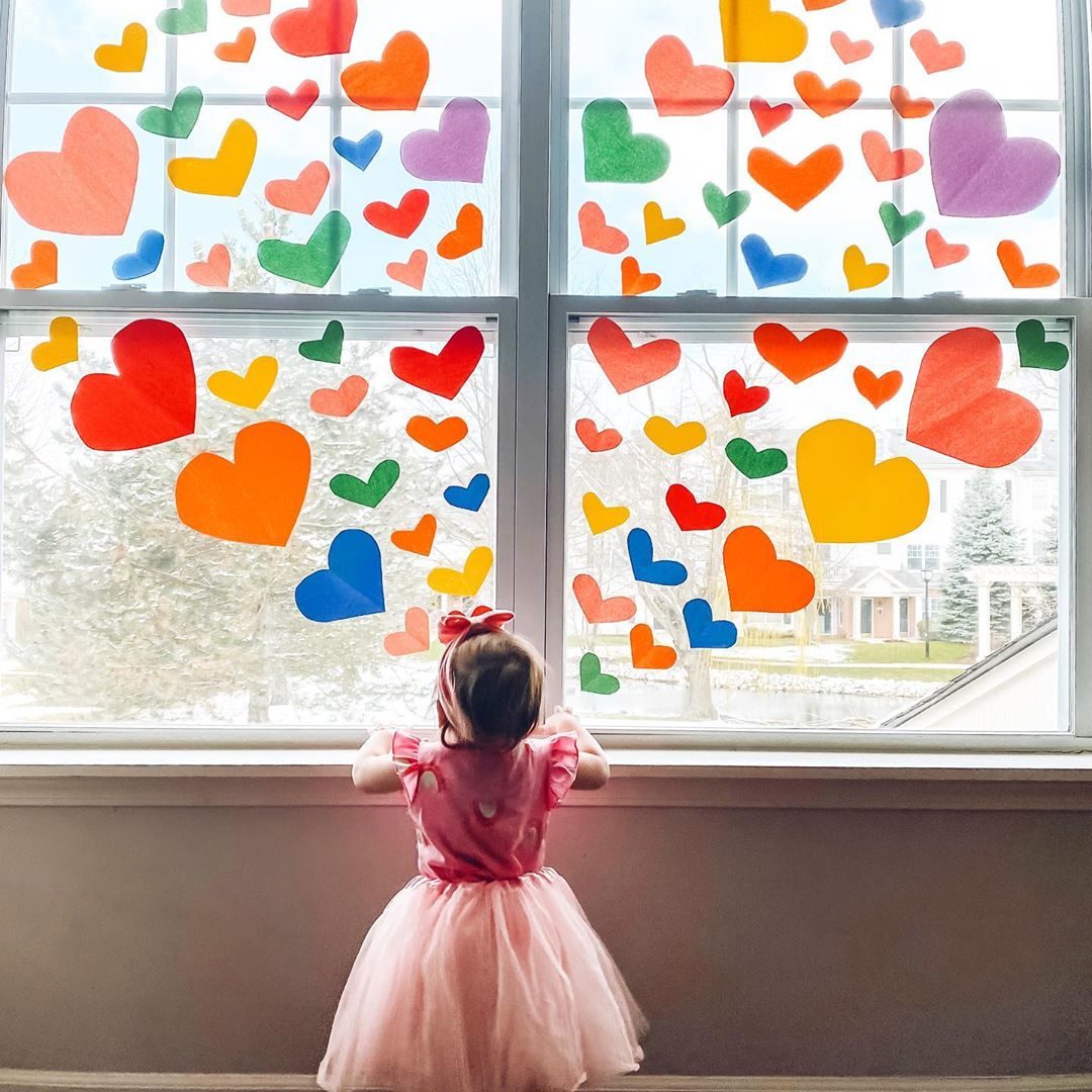 A little girl looks out a window covered in hearts of all colours of the rainbow.
