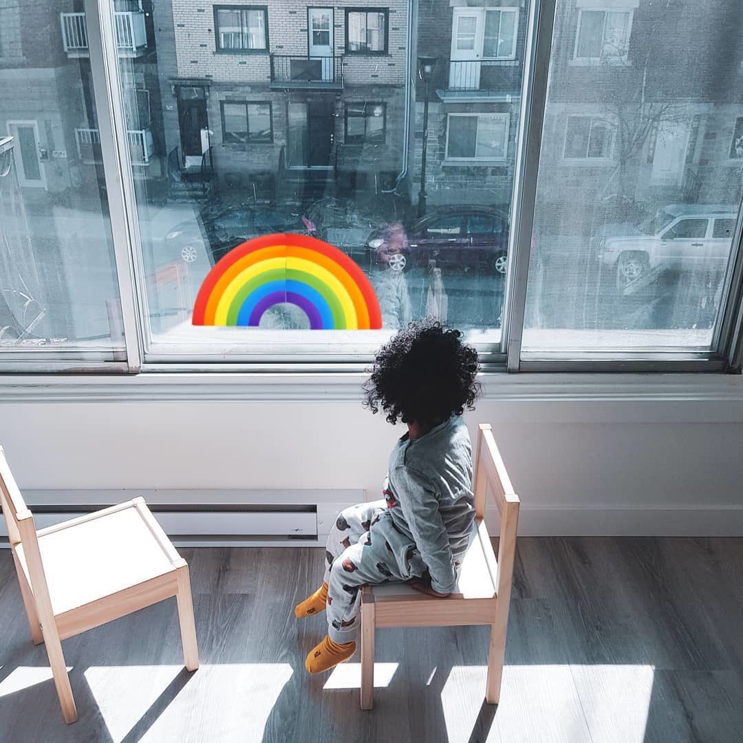 A little girl looks out a window with a rainbow on it.