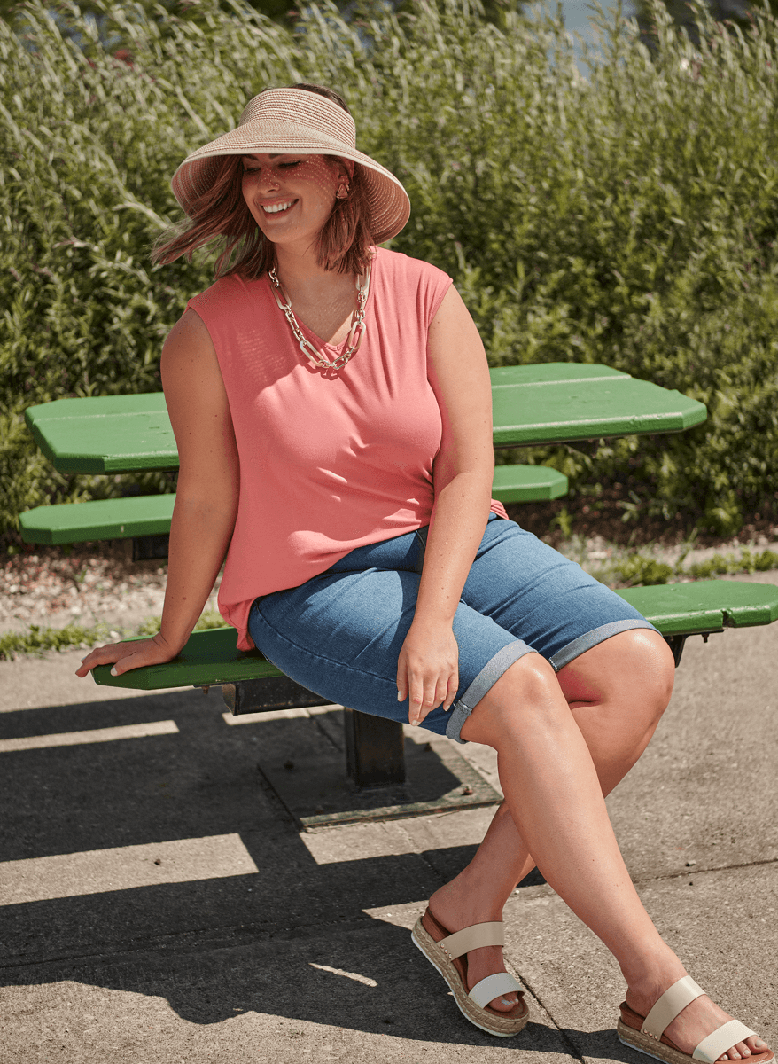 A person in a sunhat, a bright salmon top and jean shorts